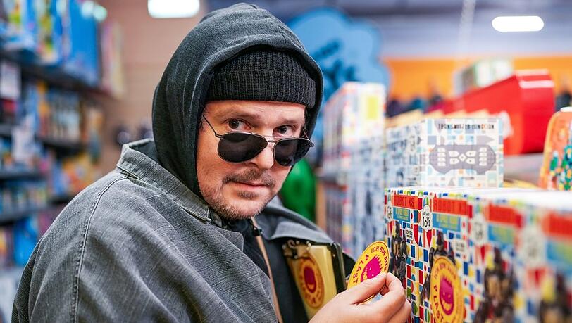 "Eigentlich sollten wir": Stefan Steindl (Thomas Mraz) klebt Plastik-Warnkleber auf Spielzeugverpackungen in einem Geschäft im Einkaufszentrum.