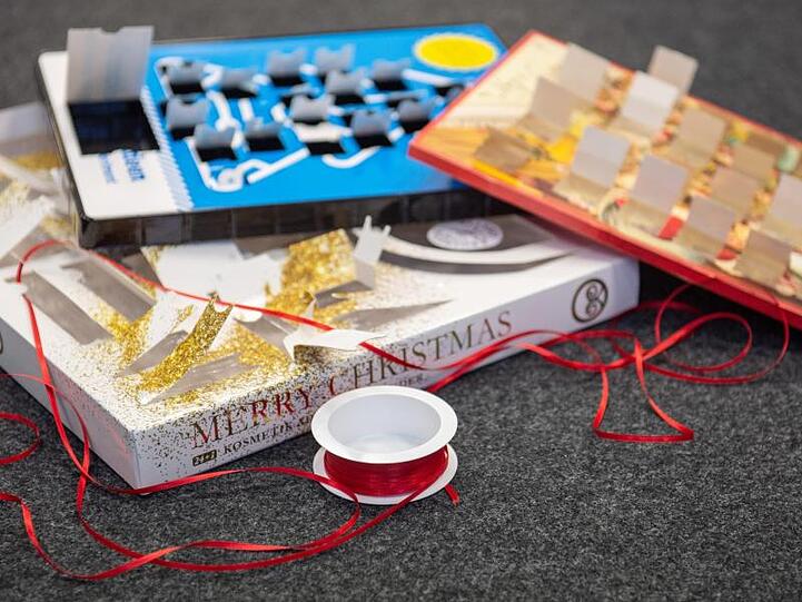 Leere Adventskalender liegen zusammen mit einer Rolle Geschenkband auf dem Boden.