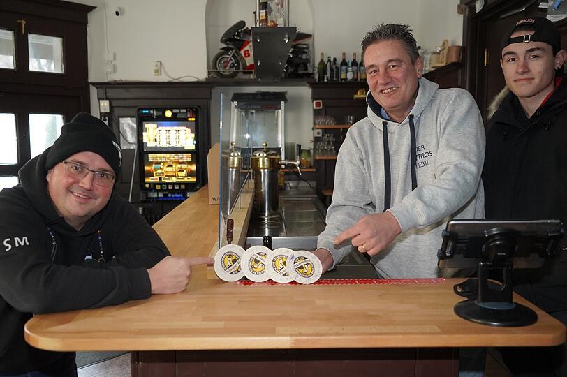 Steffen Marx (links) vom Giesinger Bräu begleicht am leeren Tresen die offenen Deckel der Bar Bajanni. Toni Valasakis und sein Sohn Leon freuen sich.