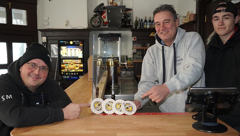 Steffen Marx (links) vom Giesinger Bräu begleicht am leeren Tresen die offenen Deckel der Bar Bajanni. Toni Valasakis und sein Sohn Leon freuen sich.
