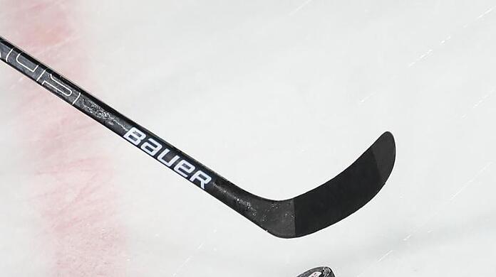Ein Puck liegt vor einem Eishockey-Schläger auf dem Eis.