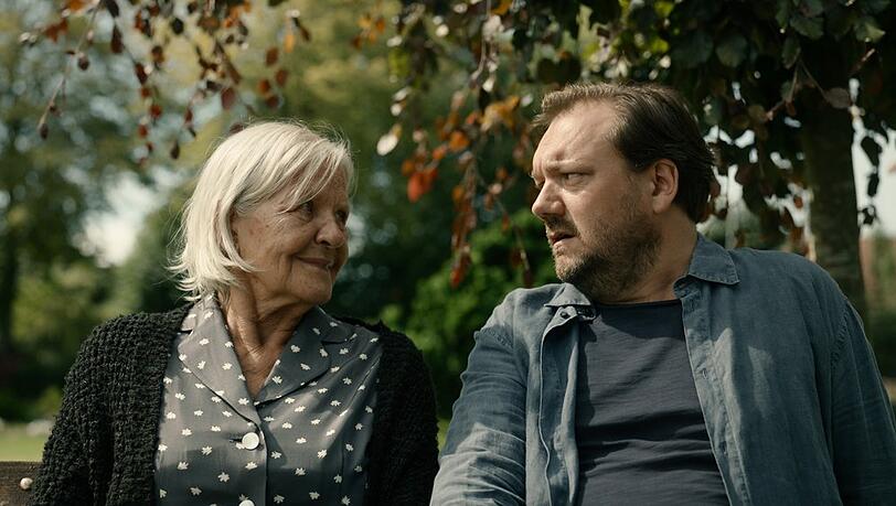 "Mittagsstunde": Ella (Hildegard Schmahl) und Ingwer Feddersen (Charly Hübner) sitzen zusammen auf einer Bank und unterhalten sich.