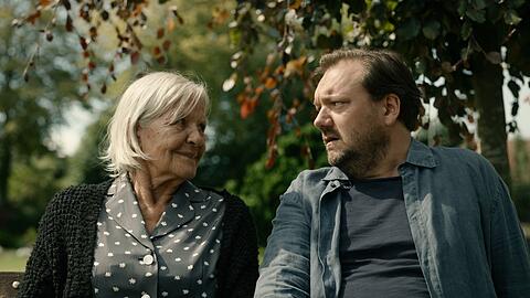 "Mittagsstunde": Ella (Hildegard Schmahl) und Ingwer Feddersen (Charly Hübner) sitzen zusammen auf einer Bank und unterhalten sich.