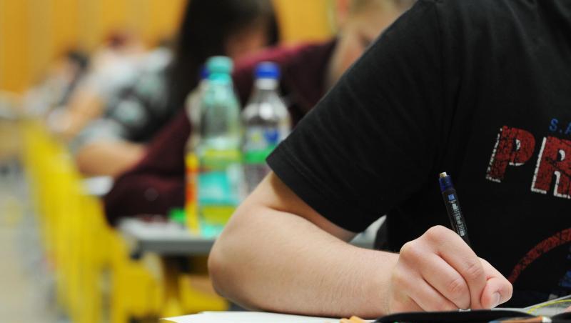 Schüler und Schülerinnen sitzen in einem Klassenraum und schreiben eine Prüfung. Die Person im Bildvordergrund hält einen Stift beim Schreiben in der rechten Hand. Foto: Armin Weigel/Archiv Schüler und Schülerinnen sitzen in einem Klassenraum und schreiben eine Prüfung. Die Person im Bildvordergrund hält einen Stift beim Schreiben in der rechten Hand. Foto: Armin Weigel/Archiv