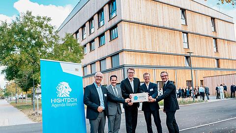 V. l.: Prof. Andreas Bausch, Co-Direktor des COS, TUM-Pr&auml;sident Prof. Thomas F. Hofmann, Wissenschaftsminister Markus Blume, Prof. Matthias Hebrok, Executive Director des COS und Co-Direktor Prof. Maximilian Reichert. Im Hintergrund: das neu errichtete Forschungslabor in Holzhybrid-Bauweise.
