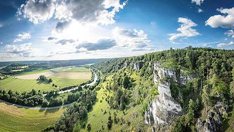 Was für ein Ausblick ins Altmühltal: Rechts ragen weiße Felsen auf, die Altmühl fließt durch Wiesen und Felder.