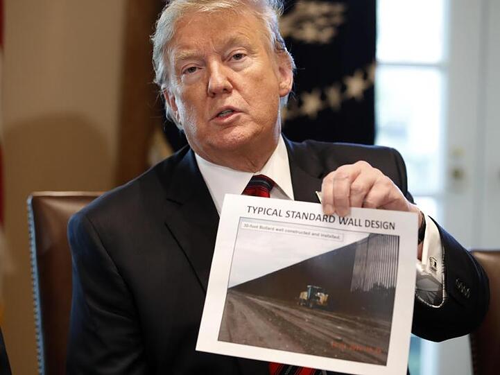 Donald Trump hält ein Foto einer möglichen Grenzmauer in der Hand.