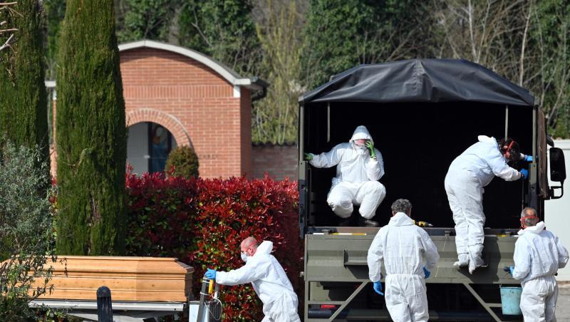 Menschen in Schutzanzügen transportieren einen Sarg auf dem Friedhof von Ferrara. Menschen in Schutzanzügen transportieren einen Sarg auf dem Friedhof von Ferrara.