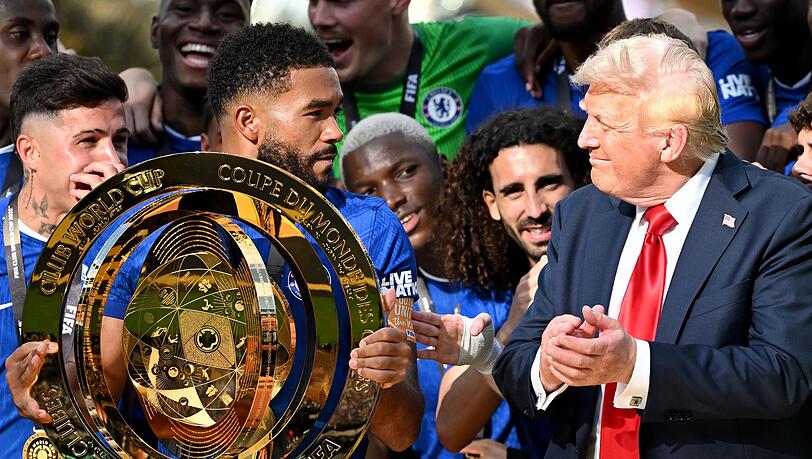 Chelseas Kapitän Reece James (l/vorn) hält auf dem Siegerpodest die Trophäe in den Händen und schaut irritiert zu US-Präsident Donald Trump.