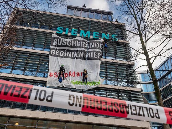 Einen Tag vor der Siemens-Hauptversammlung bringen angeseilte Aktivisten ein Transparent an die Fassade der Siemens-Zentrale in München an. Foto: Peter Kneffel/dpa