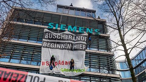 Einen Tag vor der Siemens-Hauptversammlung bringen angeseilte Aktivisten ein Transparent an die Fassade der Siemens-Zentrale in München an. Foto: Peter Kneffel/dpa
