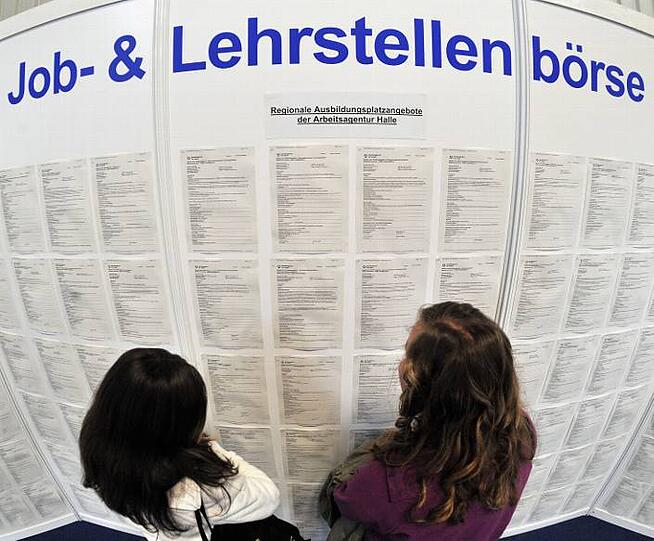 Zwei Jugendliche stehen in Halle vor einer Wand mit Job- und Lehrstellenangeboten.