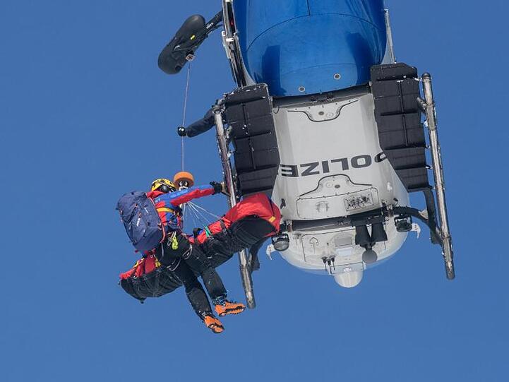 Ein Bergwachtmann und eine gerettete Person werden in einen Polizeihubschrauber gezogen. Foto: