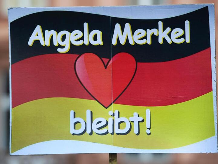 Ein Schild mit dem Schriftzug "Angela Merkel bleibt" wird vor dem Rathaus 2016 hochgehalten.