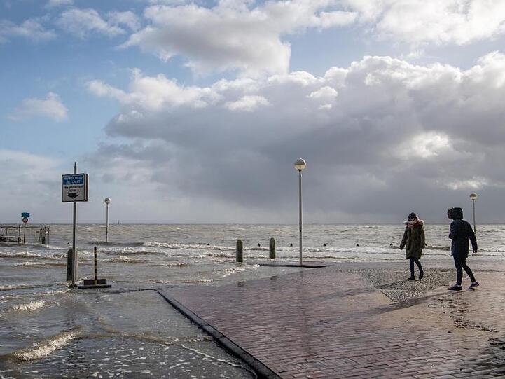 Spaziergänger laufen über einen überfluteten Parkplatz an der Nordseeküste.