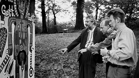 André Heller (li.) , Brian Eno und David Bowie schauen sich in Gugging die Kunst der Patienten an.