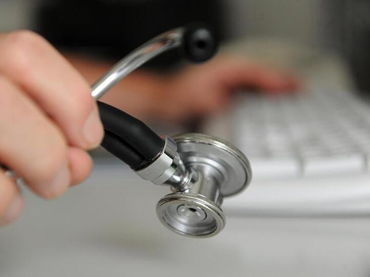 Eine Person hält ein Stethoskop in der rechten Hand. Die linke Hand bedient eine Computertastatur. Foto: Marijan Murat/Archiv