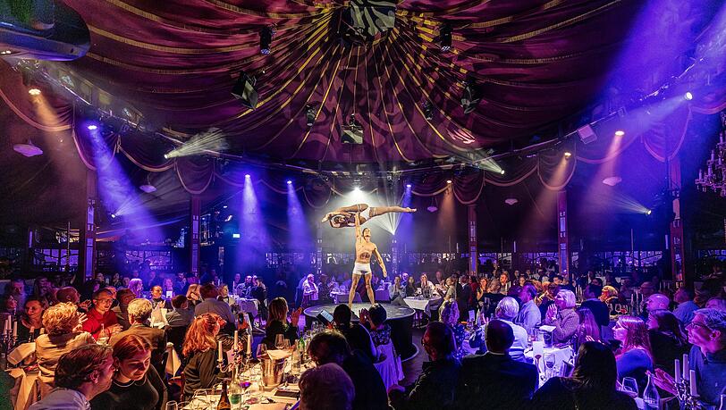 Im Spiegelzelt verfolgen die Gäste bei stimmungsvoller Beleuchtung die Show, während sie an ihren Tischen Essen und Trinken genießen. Im Spiegelzelt verfolgen die Gäste bei stimmungsvoller Beleuchtung die Show, während sie an ihren Tischen Essen und Trinken genießen.