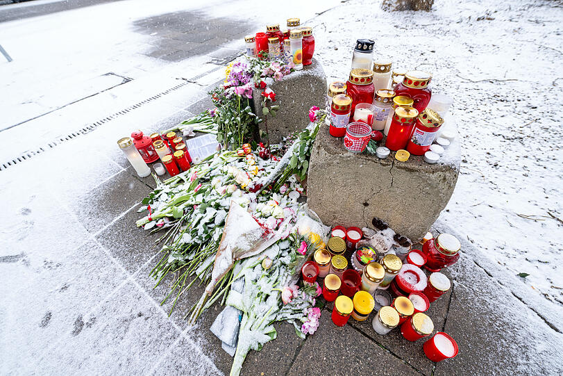 Schnee fällt auf Kerzen und Blumen, die am Straßenrand in der Nähe des Stiglmaierplatzes in München abgelegt worden sind.