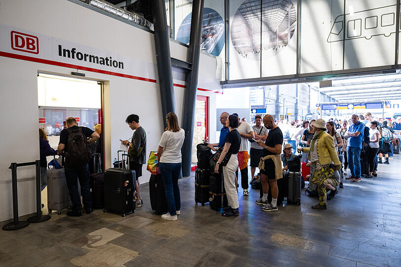 Reisende stehen im Hauptbahnhof München vor der Information in einer Schlange