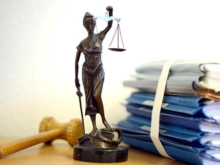 Die modellhafte Nachbildung der Justitia steht zwischen einem Holzhammer und einem Aktenstapel. Foto: Volker Hartmann/dpa/Symbolbild