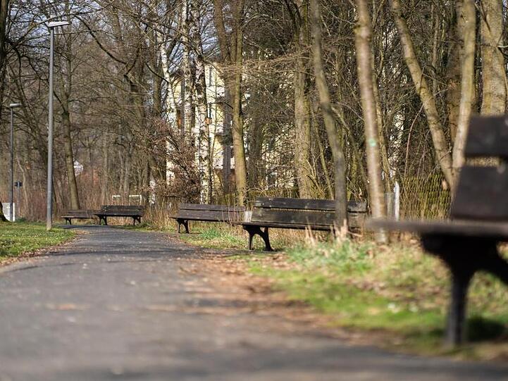 Die Sonne scheint auf leere Sitzbänke entlang eines Fußgängerweges. Foto: Nicolas Armer/dpa/Symbolbild