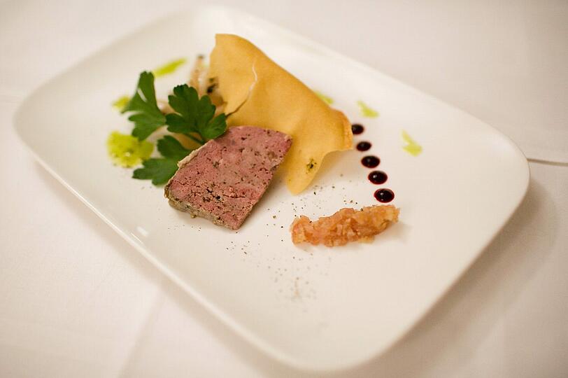 2. GANG: Provençalische Wildterrine &ndash; schwarzer Rettich &ndash; Petersilie &ndash; weißes Zwiebelconfit. Auf Filoteig gebettet, reckt sich die Terrine dem Gast entgegen. Die Terrine ist sozusagen die kleine Schwester der Pastete, zubereitet ohne Teig. Scharfe und süße Noten bringen der schwarze Rettich und das weiße Zwiebelconfit zum Reh, der Blaufränkische vom Weingut Strehn im Burgenland, Jahrgang 2012, ergänzt das Gericht mit seiner saftigen Frucht, der Würze und einer leichten Salzigkeit im Abgang.