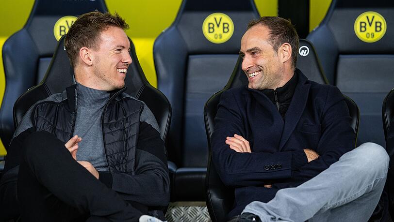 Leipzigs Trainer Julian Nagelsmann (l) und Oliver Mintzlaff, Geschäftsführer RB Leipzig sitzen vor dem Spiel auf der Trainerbank und unterhalten sich. Mintzlaff trauert dem Abgang von Nagelsmann hinterher.