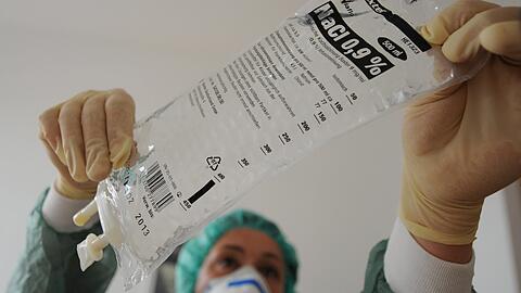 Eine Krankenschwester hängt eine Flasche mit Kochsalzlösung in einen Infusionsständer. Das Mittel ist für die Infusion unbedingt notwendig.