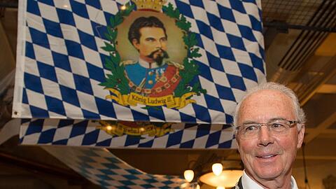 Der Kaiser und der Kini: Franz Beckenbauer vor einer Bayern-Fahne mit dem Konterfei von Märchenkönig Ludwig II..