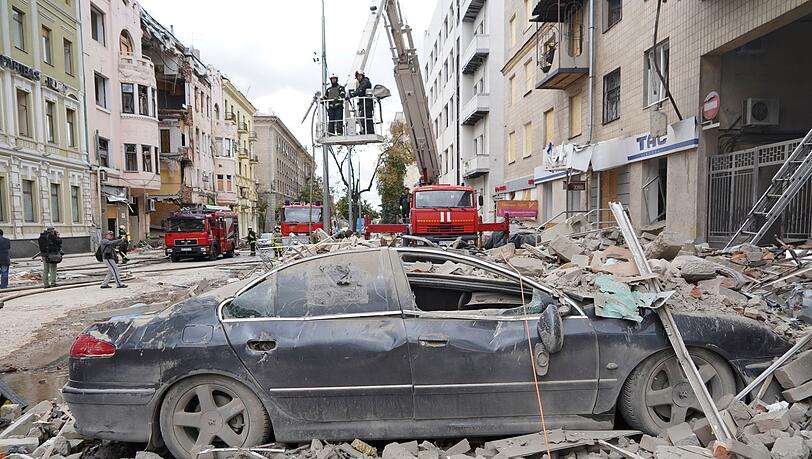 Feuerwehrleute stehen nach einem Raketenangriff des russischen Militärs auf einem Kran auf einer Straße in Charkiw.