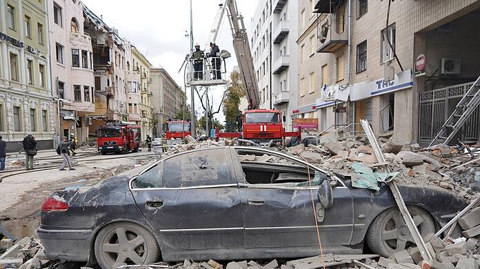 Feuerwehrleute stehen nach einem Raketenangriff des russischen Militärs auf einem Kran auf einer Straße in Charkiw.