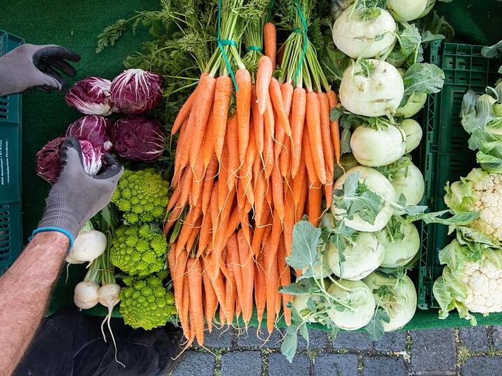 Ein Händler sortiert an seinem Verkaufsstand auf einem Wochenmarkt frisches Gemüse.