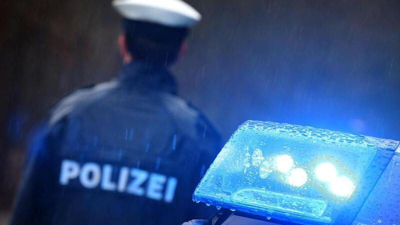 Ein Polizist steht im Regen vor einem Streifenwagen dessen Blaulicht aktiviert ist. Foto: Karl-Josef Hildenbrand/dpa/Illustration