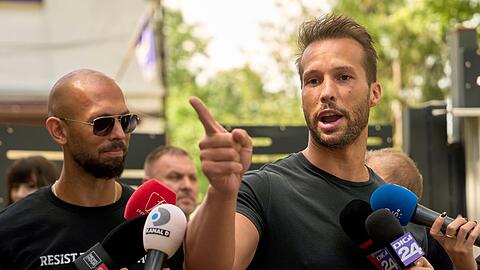 Andrew Tate (links) schaut zu seinem Bruder Tristan Tate, der am 21. Mai vor einer Polizeistation in Voluntari in Rumänien redete.