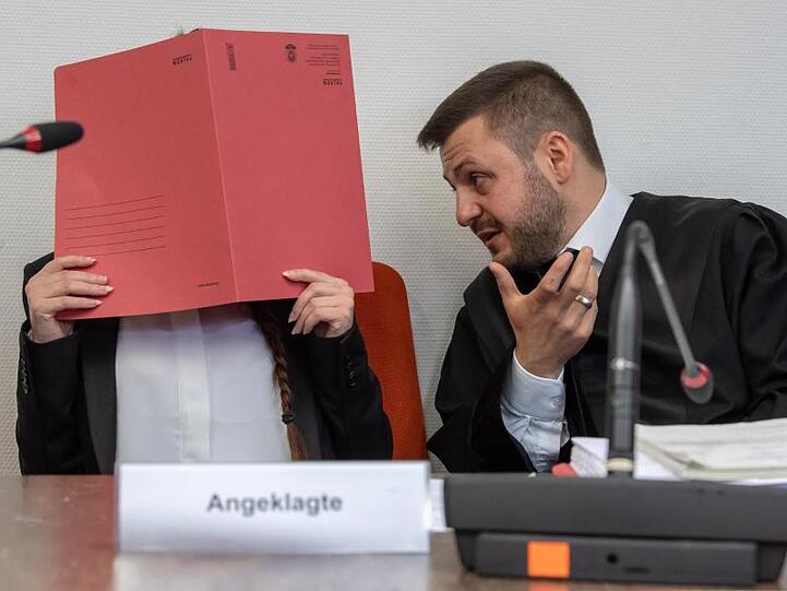 Die Angeklagte hält einen roten Aktendeckel vor ihr Gesicht. Foto: Peter Kneffel/dpa