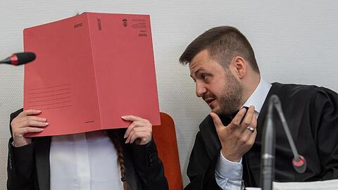 Die Angeklagte hält einen roten Aktendeckel vor ihr Gesicht. Foto: Peter Kneffel/dpa