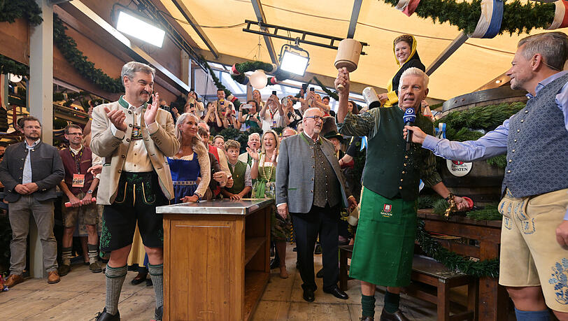 Dieter Reiter (SPD, 2.v.r), Oberbürgermeister von München, hebt seinen Anzapfschlegel nach dem Anstich des ersten Oktoberfest-Fasses im Schottenhamel-Festzelt, während Markus Söder (CSU, l), Ministerpräsident von Bayern, applaudiert.