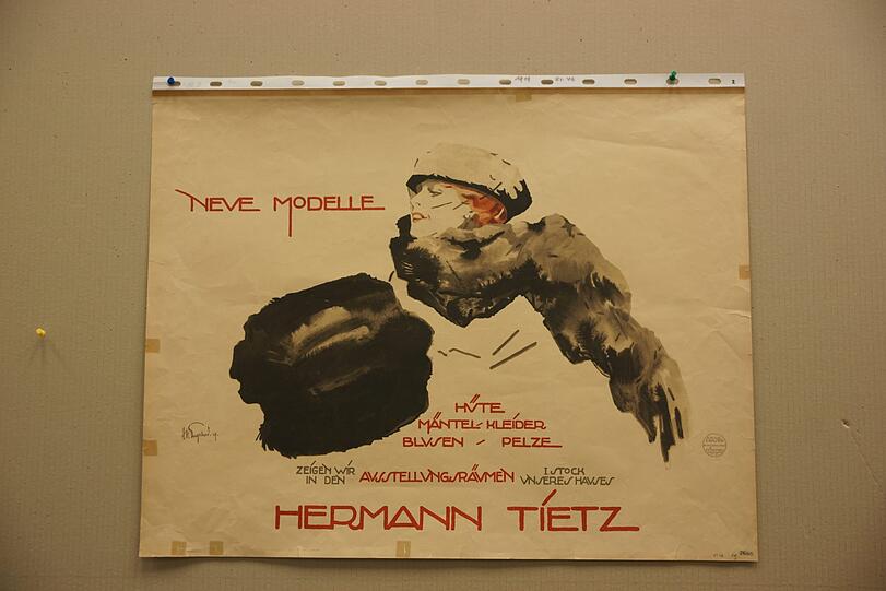 1919: "Hüte, Mäntel, Kleider, Blusen, Pelze": alles in den "Ausstellungsräumen im ersten Stock unseres Hauses Hermann Tietz" (später kurz: "Hertie") zu sehen. Dieses Plakat vom Künstler Engelhard und ist in der Grafischen Kunstanstalt von Oscar Consée in München gedruckt worden &ndash; damals in der Valleystraße 7-9. Das zeigt ein Stempel rechts unten im Bild.