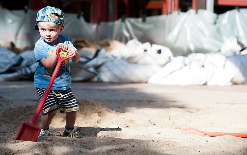Er hilft auch mit: Der kleine Henry gräbt mit einer Schaufel im Sand. Die Erwachsenen befüllen Sandsäcke...