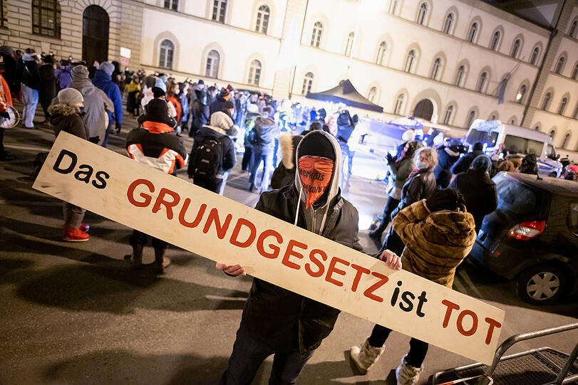Ein Versammlungsteilnehmer trägt bei einer Demonstration der Querdenken-Bewegung vor dem Bayerischer Verwaltungsgerichtshof einen Schal mit der Aufschrift "Merkels Maulkorb" und ein Schild mit der Aufschrift "Das Grundgesetz ist tot".