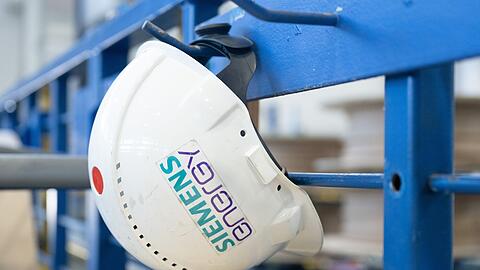Ein Schutzhelm mit der Aufschrift "Siemens Energy" hängt in einer Werkhalle.