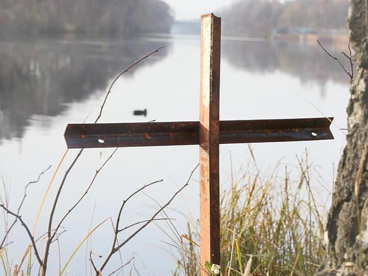 Ein zusammengeschweißtes Metallkreuz steht an einem Gewässer. Foto: Stephanie Pilick