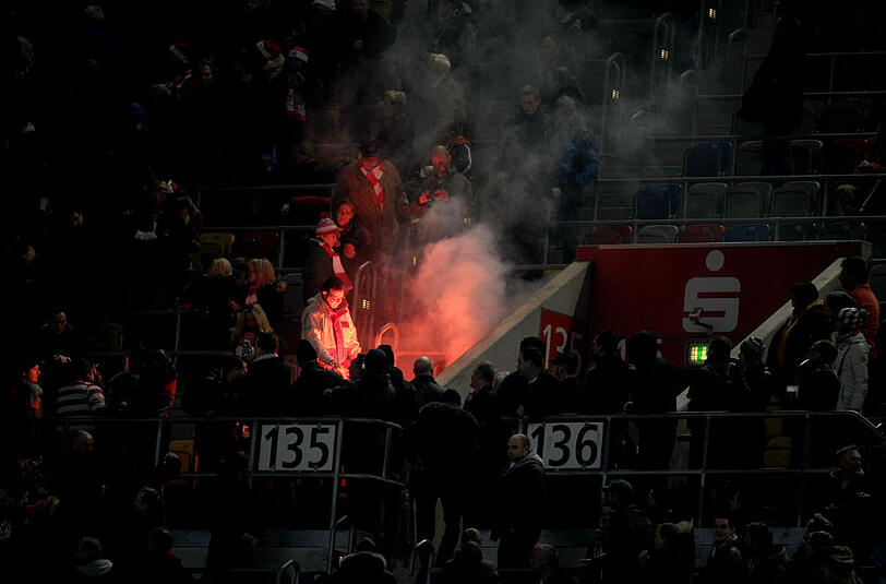 Kölner Fans werfen einen Feuerwerkskörper in den Düsseldorfer Fanbereich. Bei einem ähnlichen Vorfall im Februar 2014 wurden sieben Zuschauer verletzt. Der 1. FC Köln musste eine Strafe zahlen und fordert vom Böllerwerfer Schadenersatz.