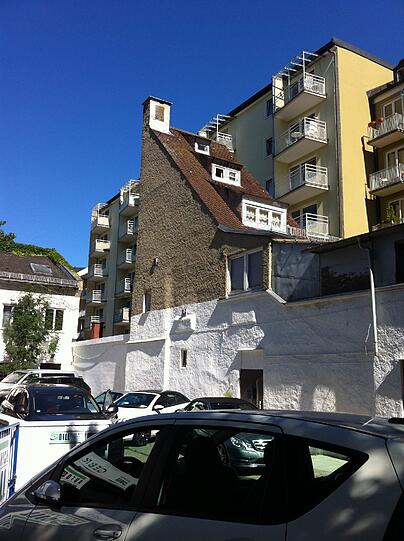 Dahinter: ein Wohnblock aus der Nachkriegszeit. Gerade dieser Gegensatz verleiht dem kleinen, alten Häuschen noch mehr Charme.