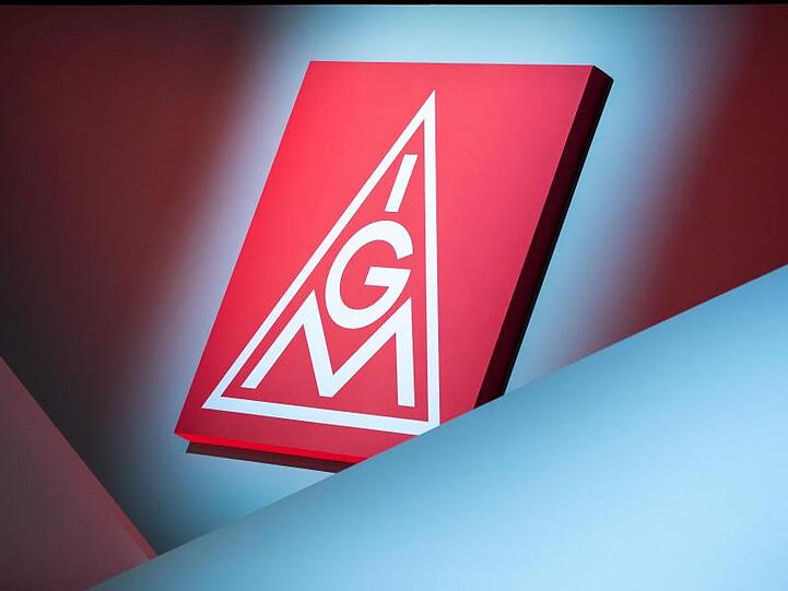 Das Logo der IG Metall hängt über einer Bühne. Foto: Daniel Karmann/dpa/Symbolbild