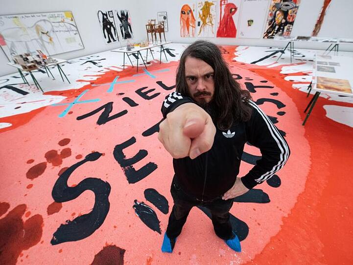Jonathan Meese, Maler und Aktionskünstler, steht bei einem Interviewtermin in dem noch geschlossenen Ausstellungsraum. Foto: Lino Mirgeler