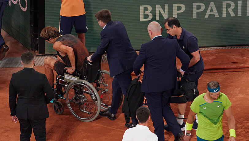 Alexander Zverev wird im Rollstuhl vom Court gefahren.
