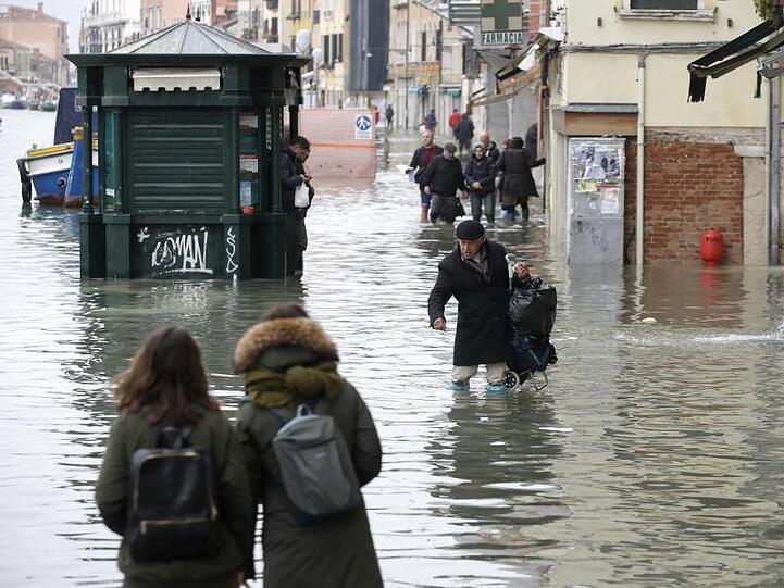 Menschen waten durch eine überflutete Straße. Bürgermeister Luigi Brugnaro spricht von einer "Katastrophe" und macht den Klimawandel für das Hochwassser verantwortlich.