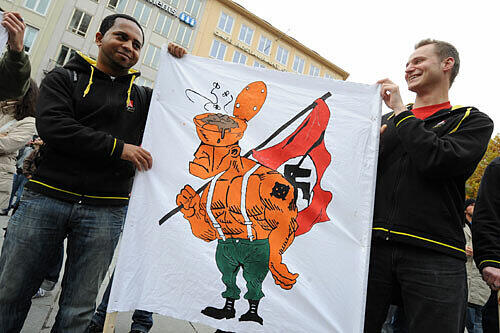 Zwei junge Männer tragen eine Karikatur gegen Nazis bei der Protestdemo gegen den &bdquo;Heldengedenkmarsch&ldquo; im vorigen Jahr.
